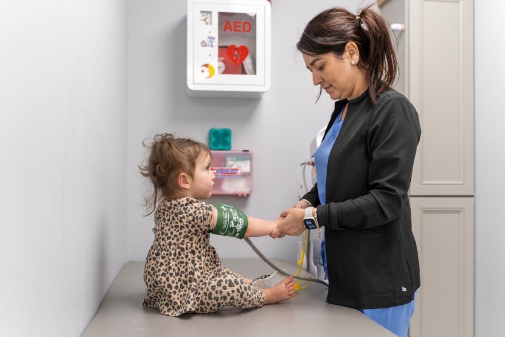 A nurse in black scrubs taking a toddler's blood pressure in an exam room at Little Giants PPEC in Tampa