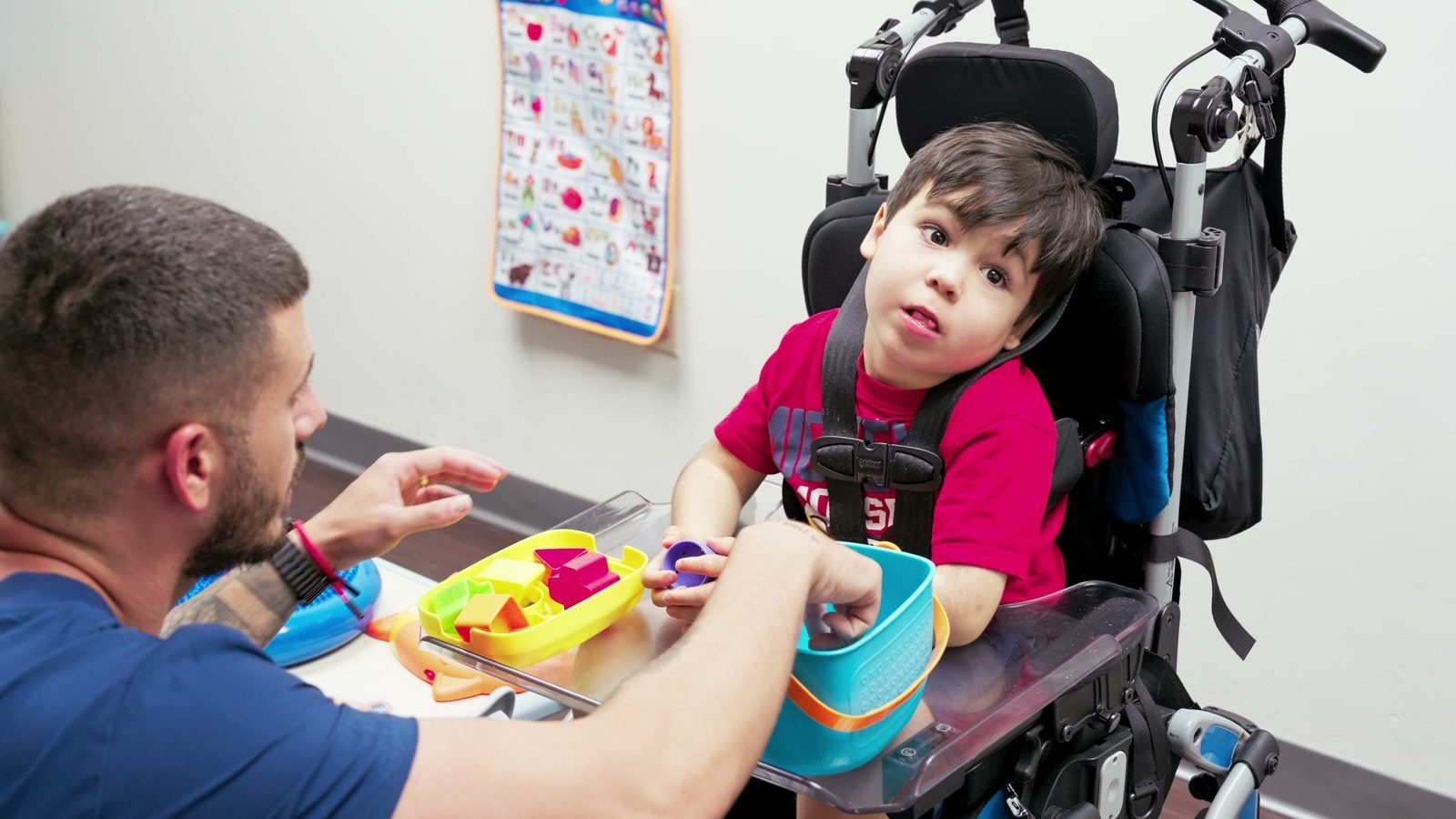 Staff member playing with a boy seated in an adaptive support chair at Little Giants PPEC in Tampa, FL