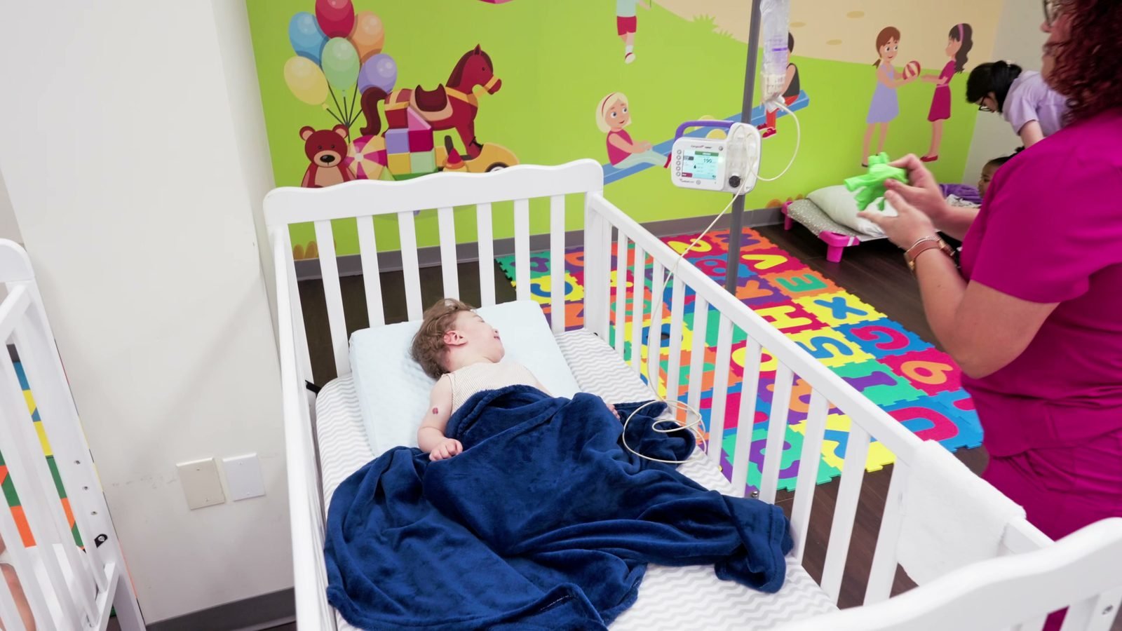 Child resting under a blanket in a crib while a nurse checks on them at Little Giants PPEC in Tampa, FL