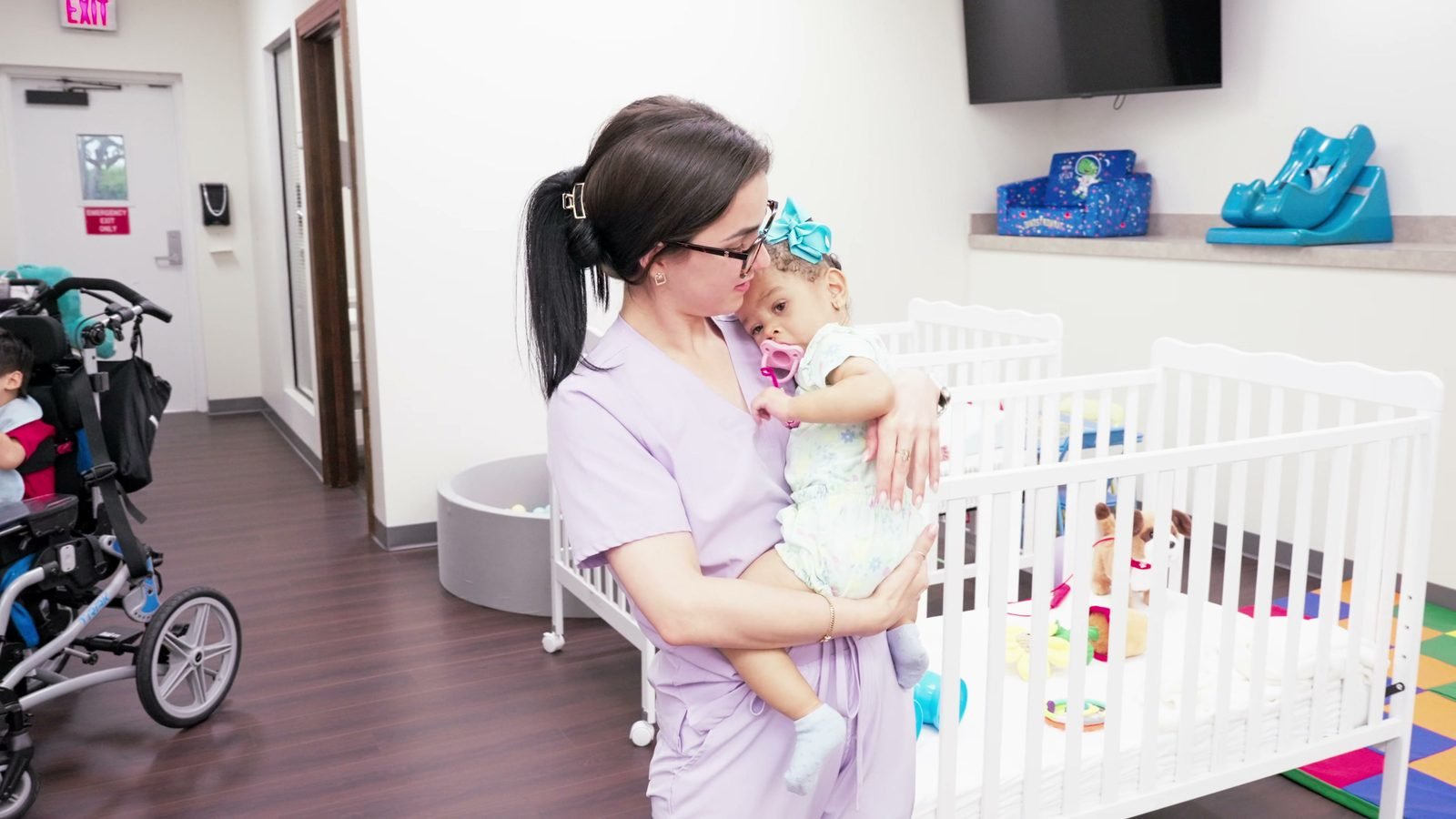 Nurse holding a baby in the nursery beside white cribs at Little Giants PPEC in Tampa, FL