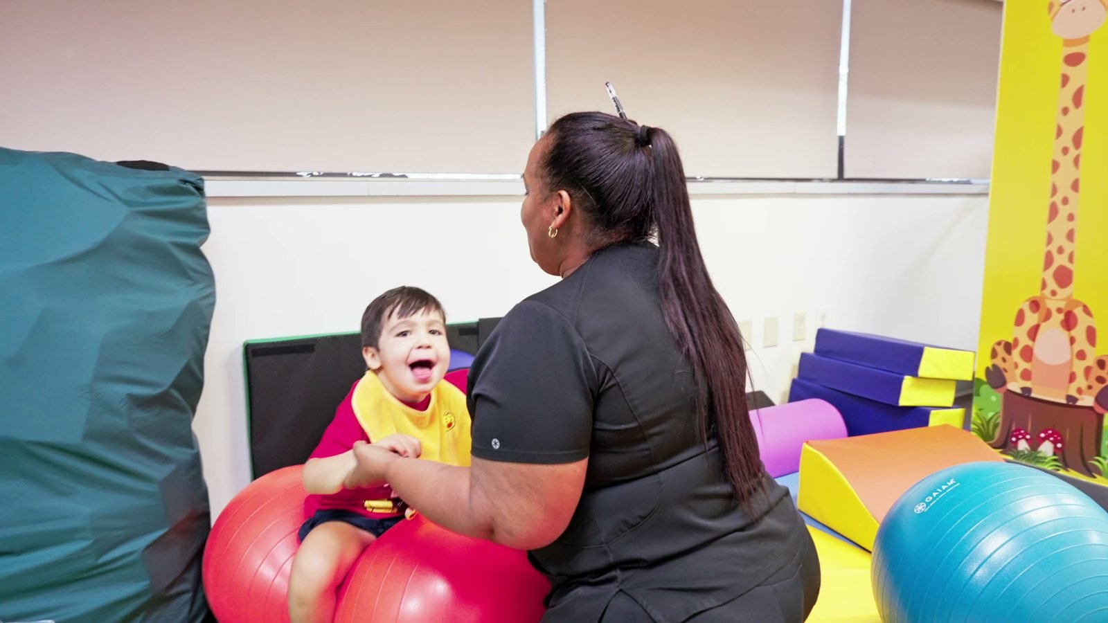Smiling boy working on balance on a therapy ball with a staff member at Little Giants PPEC in Tampa, FL