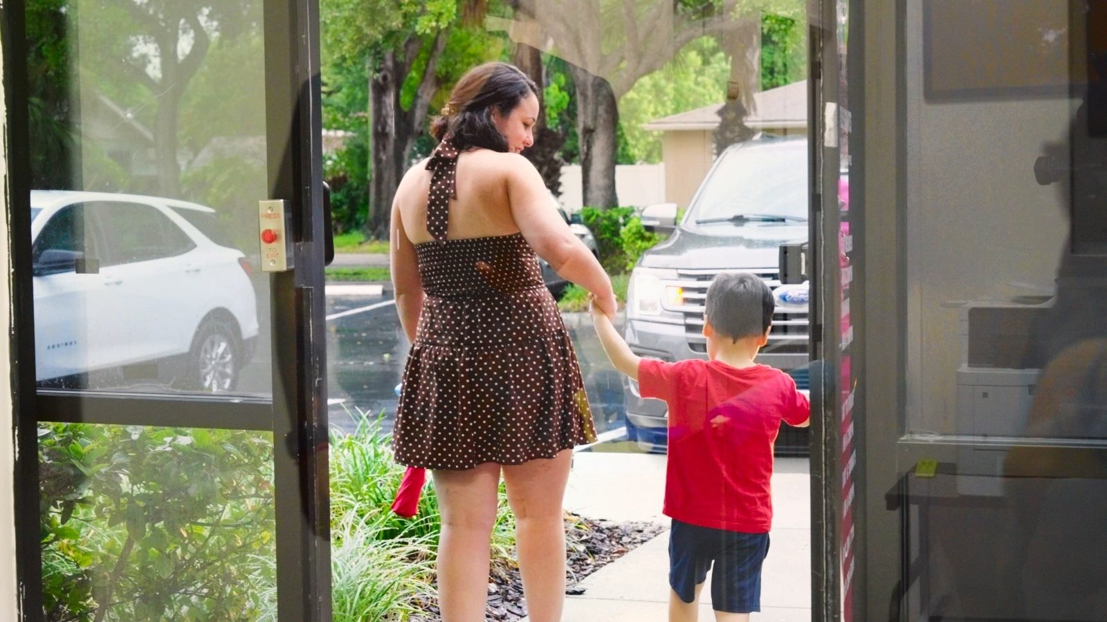 Parent holding a young boy's hand at the glass front door of Little Giants PPEC in Tampa, FL