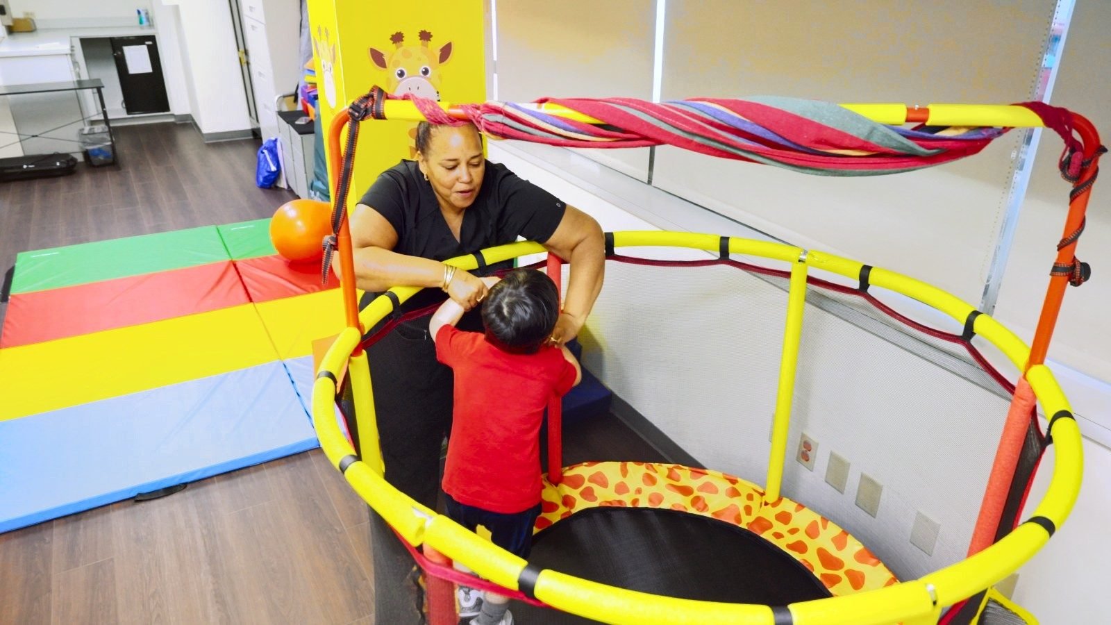 Staff member supporting a boy inside a padded mini trampoline in the play gym at Little Giants PPEC in Tampa, FL