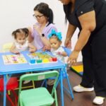 Two staff members helping two toddlers with wooden puzzles at a small blue table at Little Giants PPEC in Tampa, FL